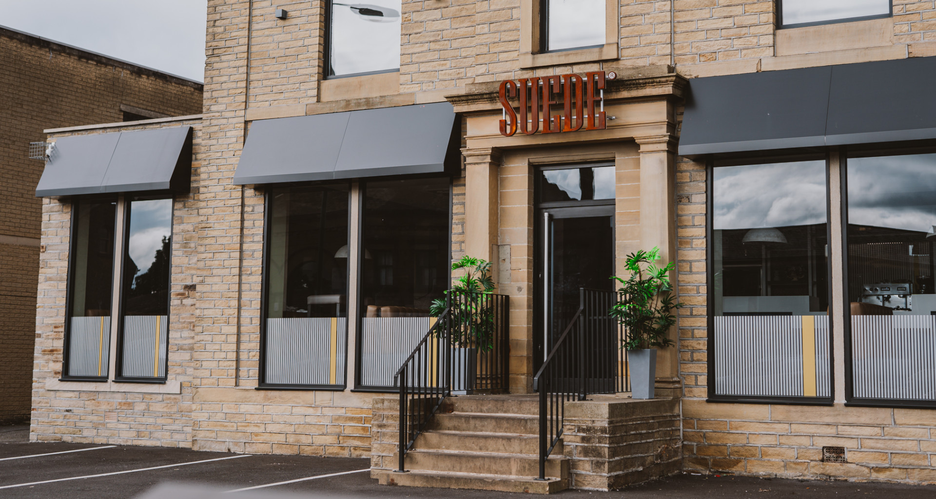 A modern restaurant exterior with a brick facade, large windows, and a sign reading 'SUEDE'.