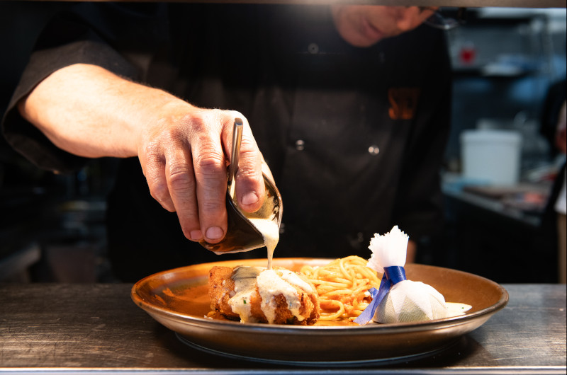 A chef drizzling sauce on a plated dish of spaghetti and meat.